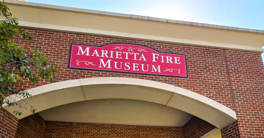 Red Marietta Fire Museum building sign mounted above the entrance on a brick exterior in Marietta, GA.