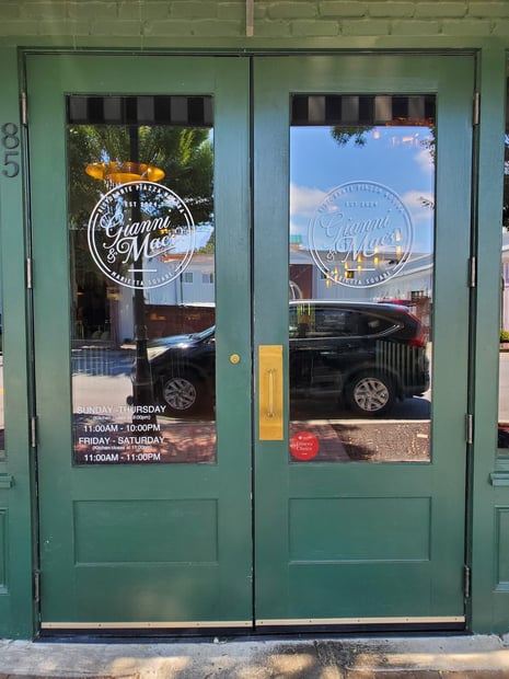 "Window graphics and decals example on restaurant storefront doors showingbranded logo design and buiness hours