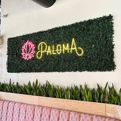 Paloma LED neon script logo with pink flower on a greenery wall inside a Marietta, GA venue—installed by Marietta Signs.